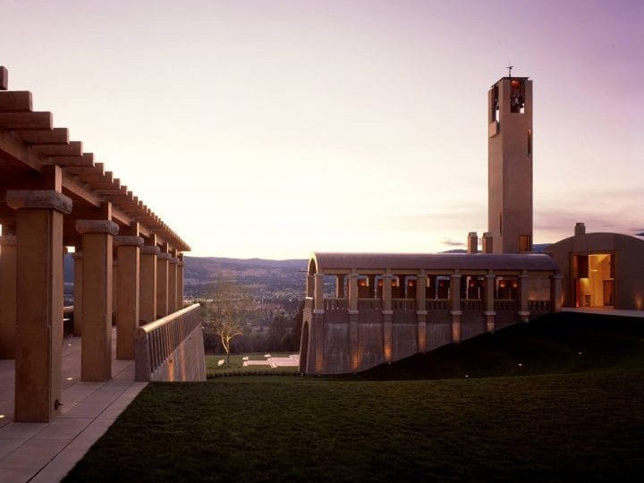 The Mission Hill Family Estate at dusk, featuring a tall bell tower, terraced walkways, and a hillside complex overlooking the Okanagan Valley.