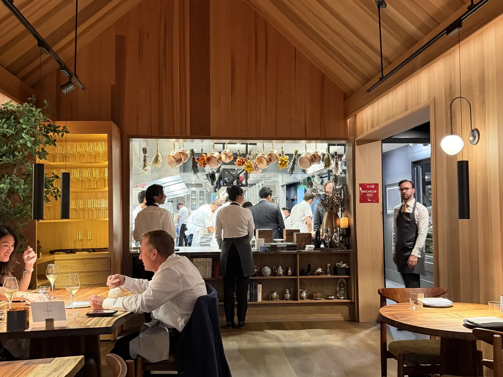 Thirty-seat Enclos dining room with a warm wood ceiling and visible open kitchen