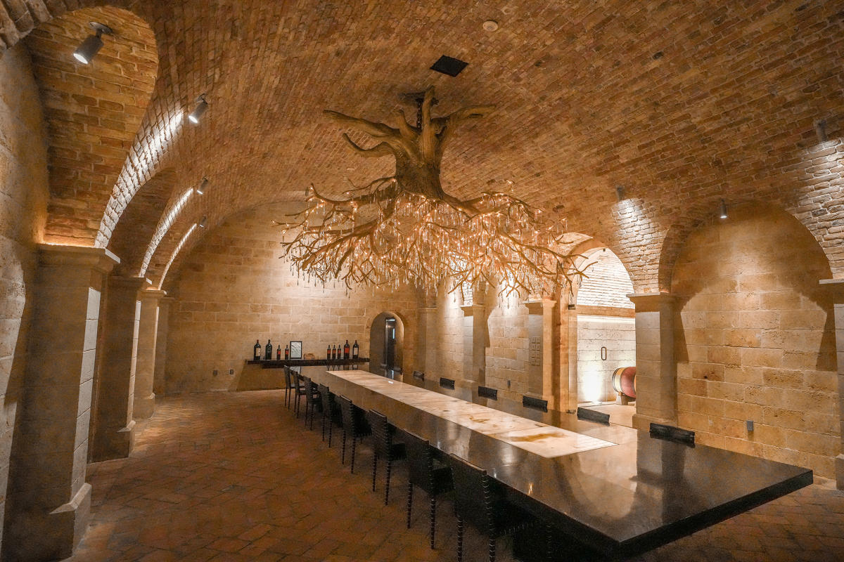 Wine tasting room with a long table, brick arches, and a decorative chandelier.