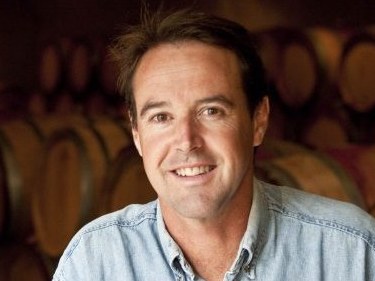 Man in denim shirt smiling in a cellar with barrels.