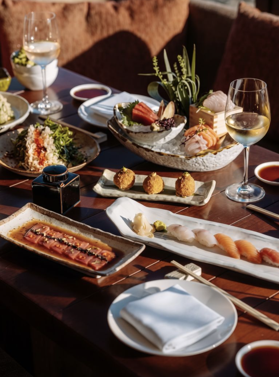 An upscale restaurant table spread featuring sushi, sashimi, fried appetizers, and white wine in an elegant dining setting