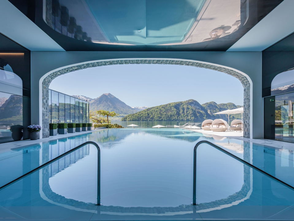 A luxury spa indoor swimming pool with arched architecture, reflective ceiling, mountain views through large opening, and handrails entering the water
