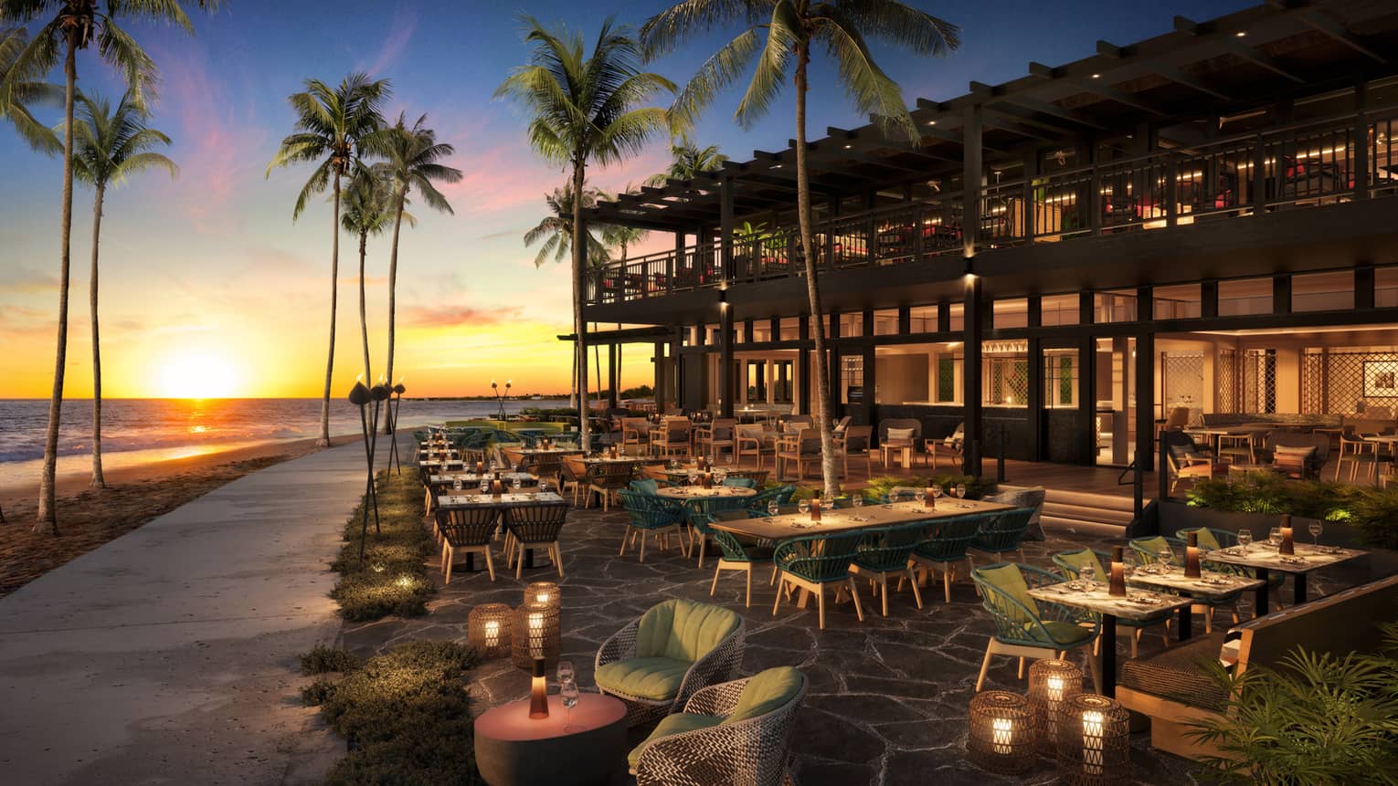 A two-story restaurant with outdoor seating at sunset, featuring palm trees and a beach with the ocean in the background.