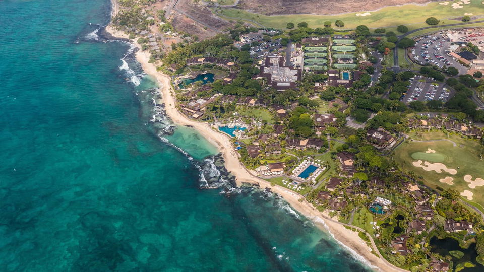 An aerial view of the Four Seasons Hualalai resort, showing its beachfront location, multiple swimming pools, golf course, and various buildings