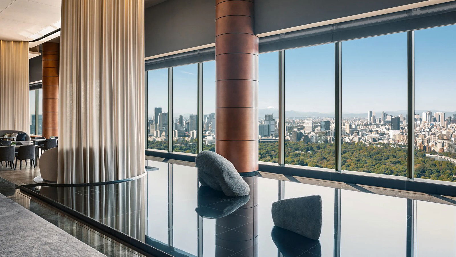 A high-floor luxury hotel interior with floor-to-ceiling windows overlooking Tokyo's skyline and the Imperial Palace Gardens.