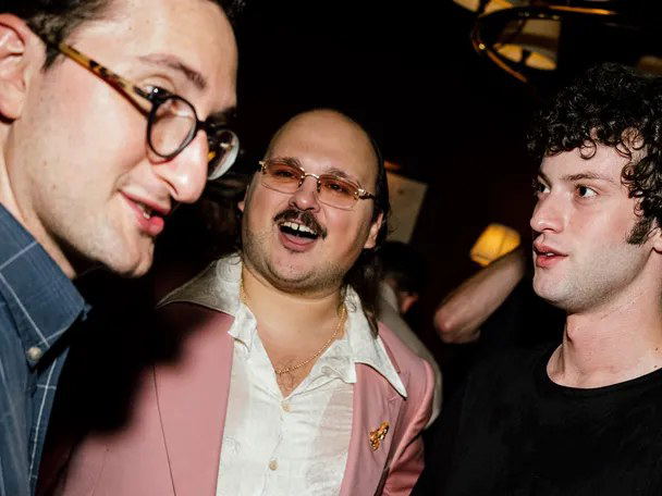 Guests at a casual party, holding drinks and socializing.
