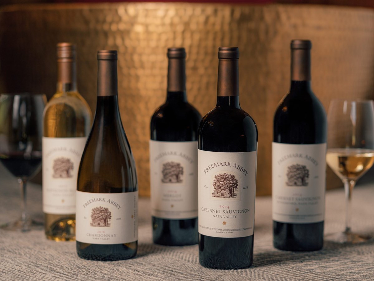 Five Freemark Abbey wine bottles, including Chardonnay and Cabernet Sauvignon, with two wine glasses on a patterned surface.