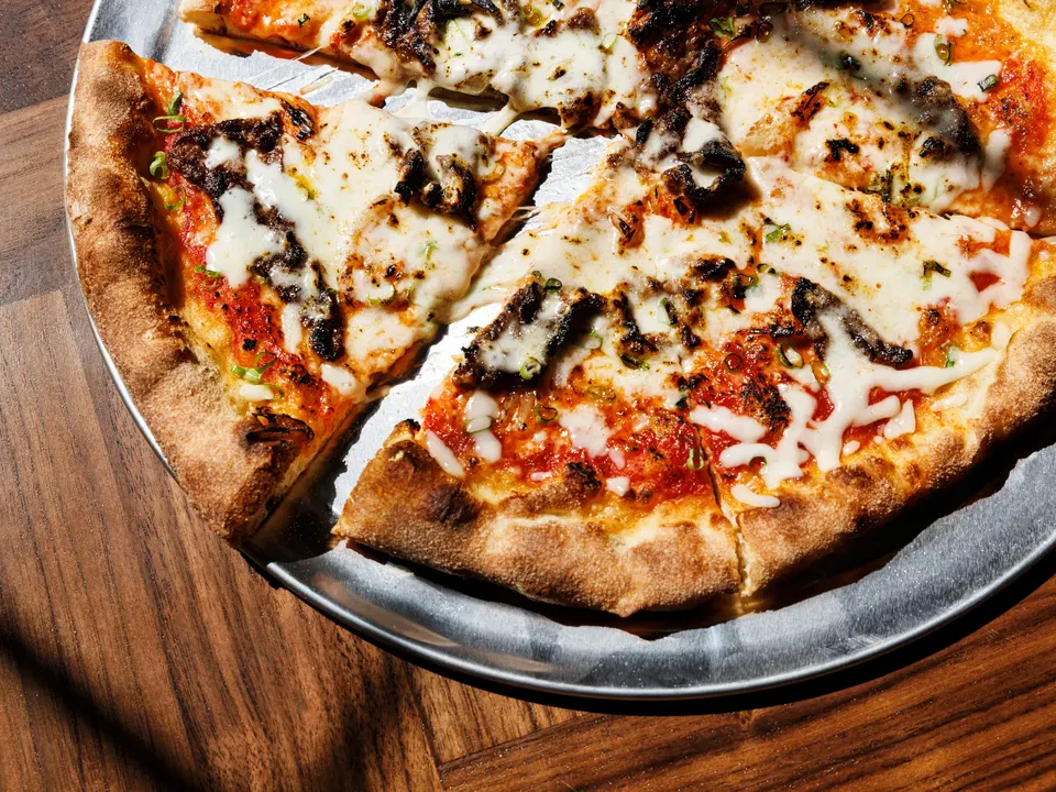 A freshly baked pizza with white cheese, red sauce, and charred spots on a wooden serving board.