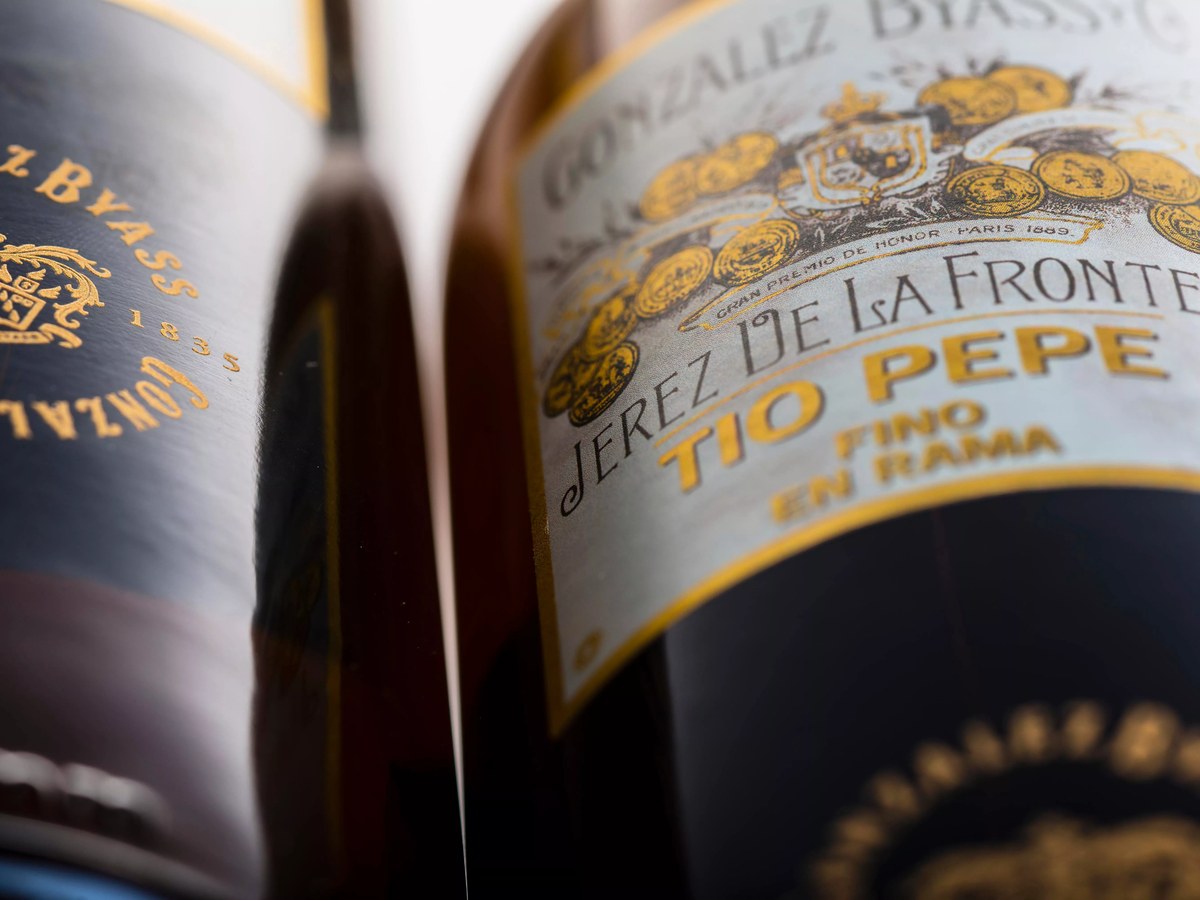 Close-up of two dark glass bottles with gold labels. The foreground bottle clearly shows 'Jerez de la Frontera Tio Pepe Fino En Rama'.