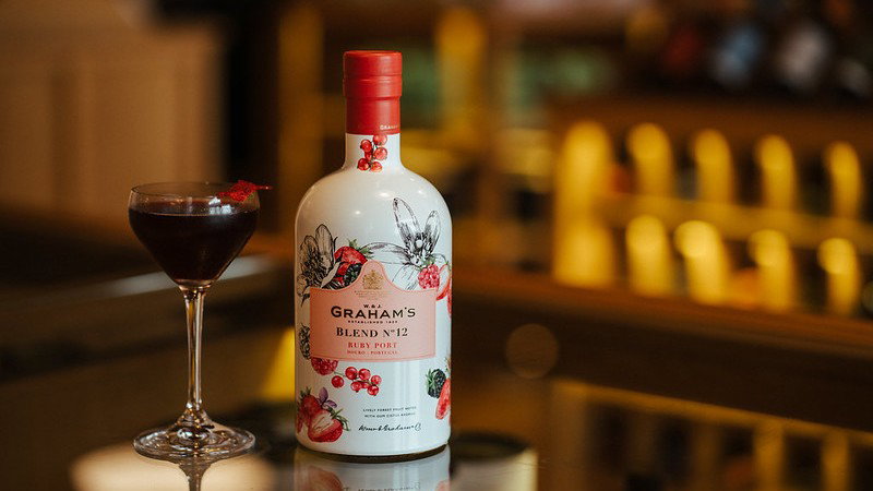 Damian Murgatroyd double-straining his Graham's Kitchen Flip cocktail into coupe glasses at the bar