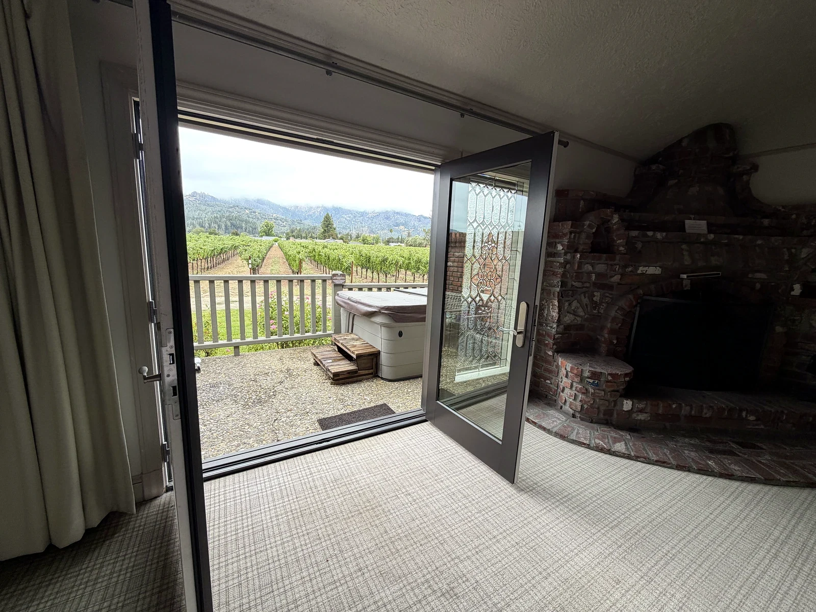 Open doors connecting a Harvest Inn fireplace room to its private hot tub and vineyard view