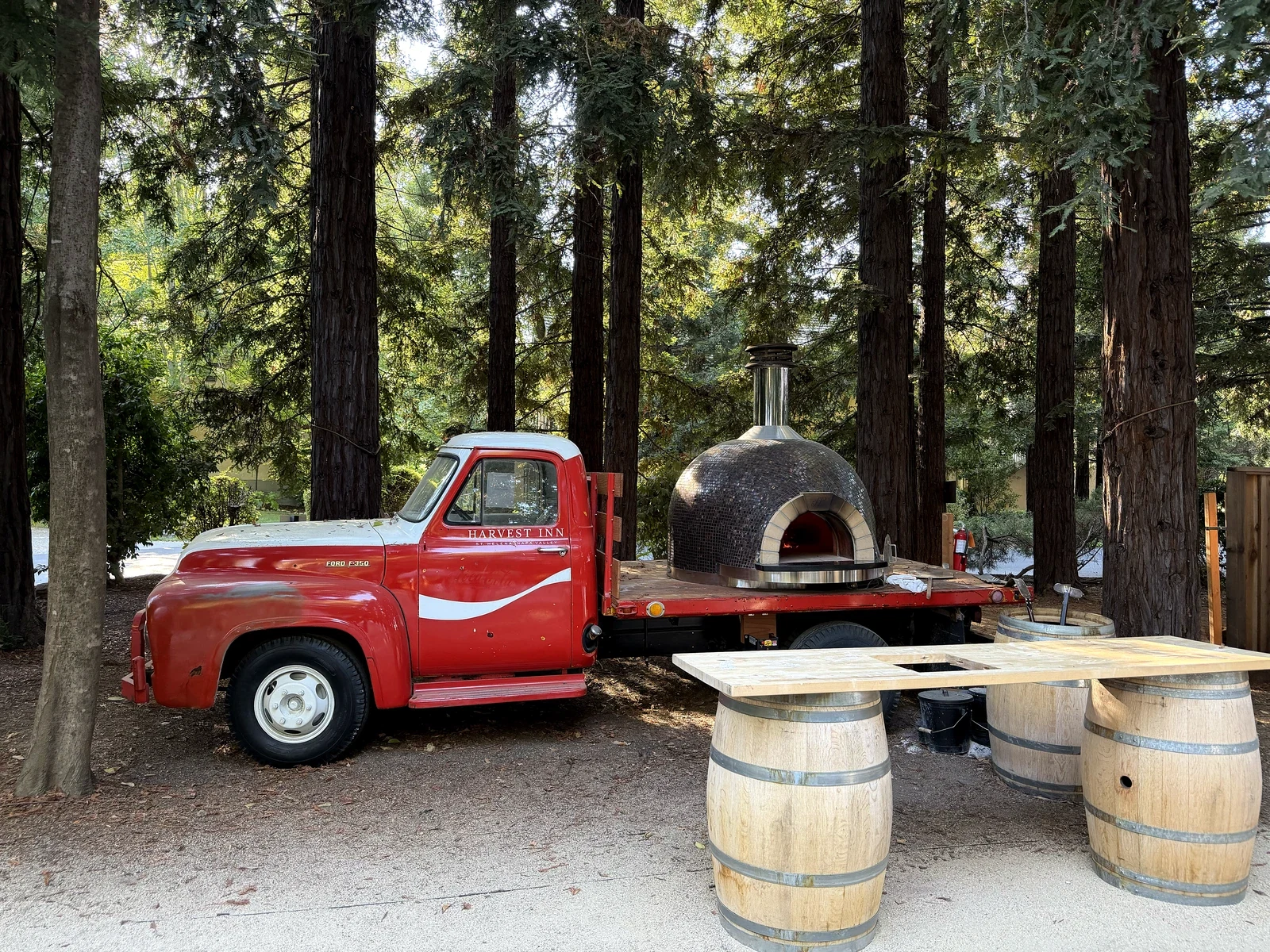 Red vintage truck carrying a domed pizza oven beneath redwoods at Harvest Inn