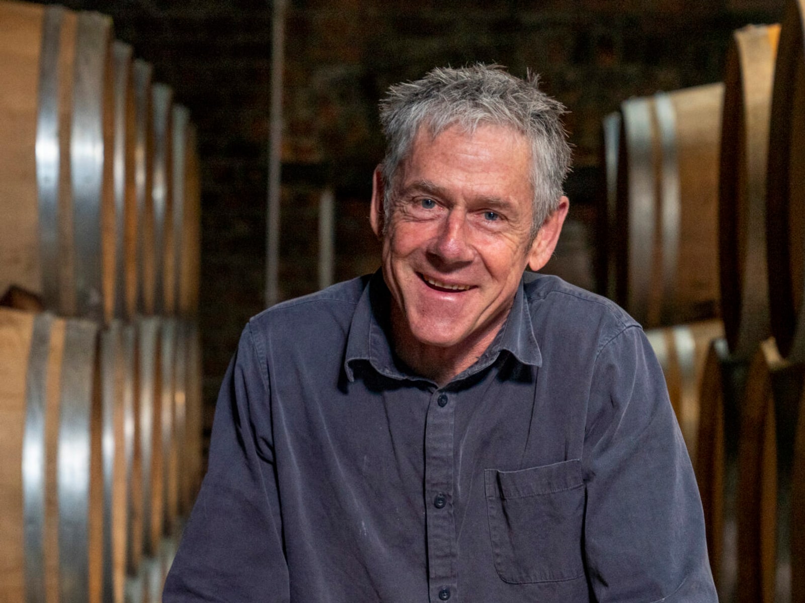 Senior winemaker Phil Brodie of Te Mata Estate smiles in a winery barrel hall, leaning over an oak barrel.