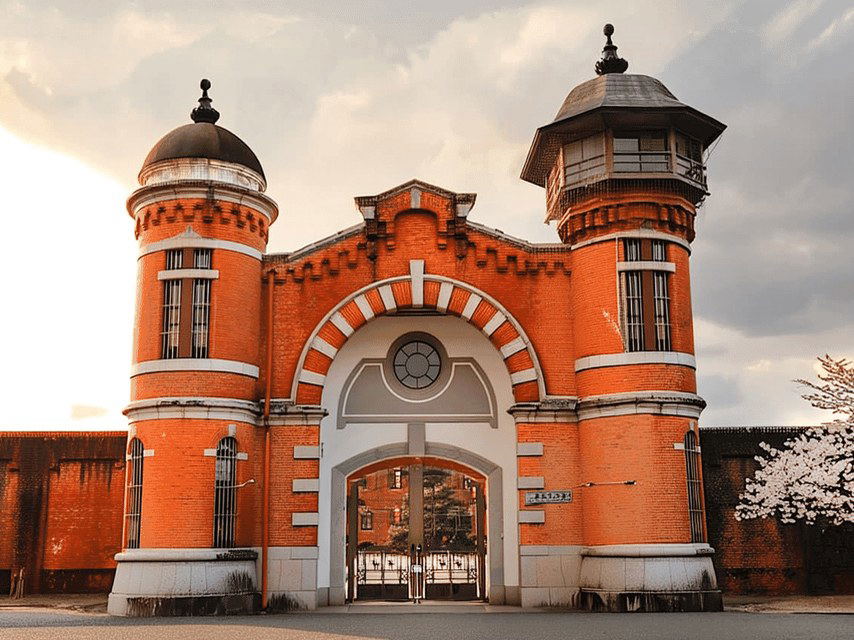 The red-brick facade of the former Nara Prison, designed by Keijiro Yamashita, features two cylindrical towers and an arched gateway under a cloudy