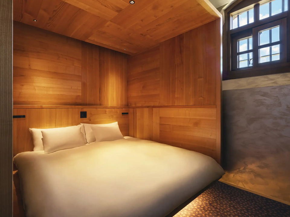 A luxury hotel bedroom with extensive wood paneling on walls and ceiling, featuring a bed with white linens and a narrow window with dark framing.