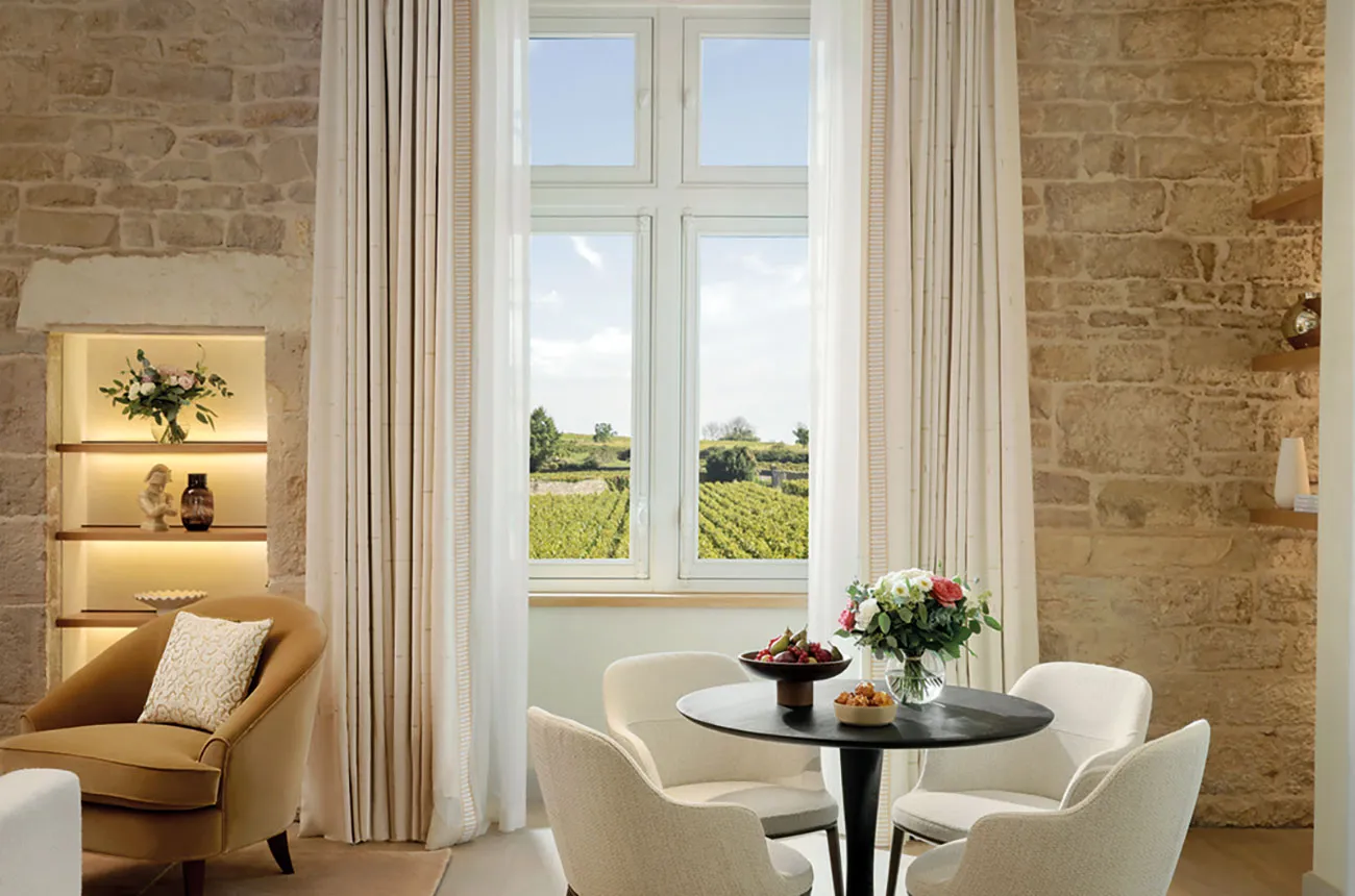 An elegant hotel lounge or sitting area with exposed stone walls, built-in illuminated shelving, contemporary furniture, a round black table with flow