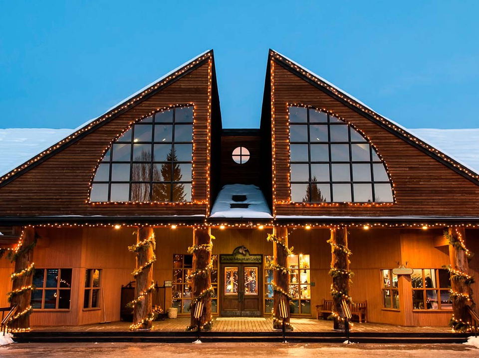 The exterior of Grouse Mountain Lodge at twilight, adorned with Christmas lights and garland, with snow on the roof and a visible sign.