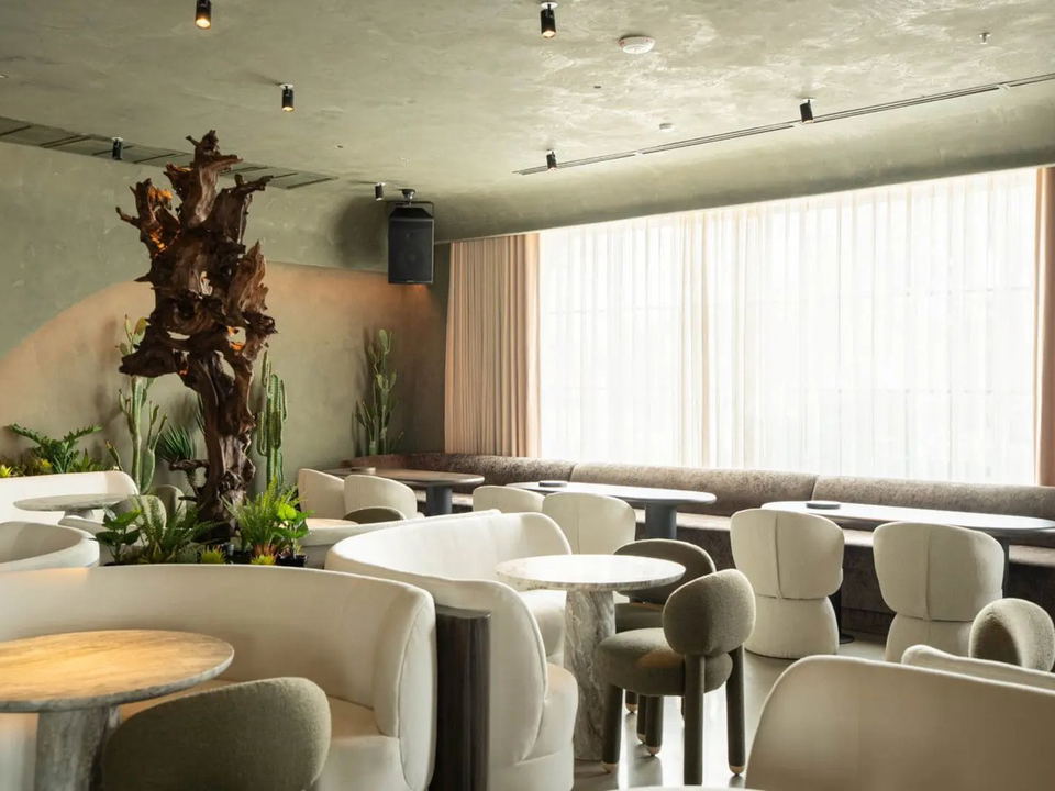 An interior shot of 1111 Westheimer, showing cream bouclé lounge chairs, marble-topped tables, and a large driftwood sculpture.