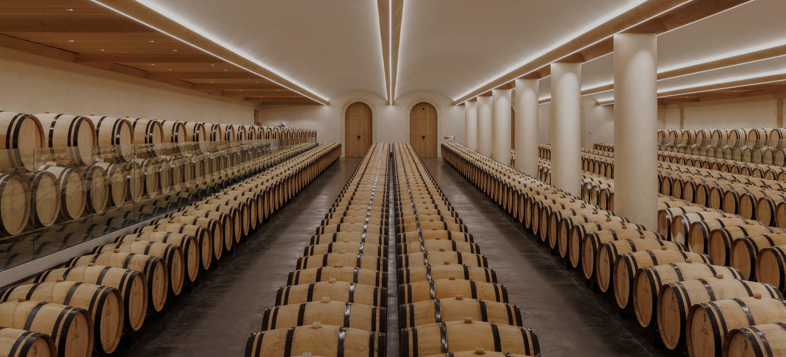 A modern barrel cellar with rows of oak wine barrels, white columns, and arched doorways