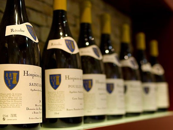 A row of bottled Hospices de Beaune wines, including Saint-Romain and Pouilly cuvées, on a shelf.