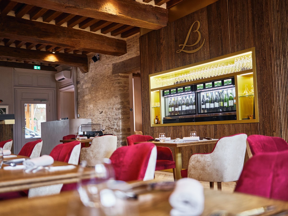 An elegant dining room at Loiseau des Vignes in Beaune, featuring red and cream chairs, wooden tables, and a backlit wine display.