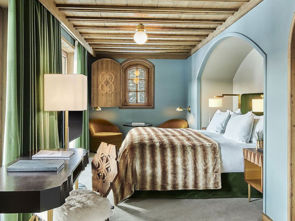 Hotel room with a bed, desk, lamp, and green curtains.
