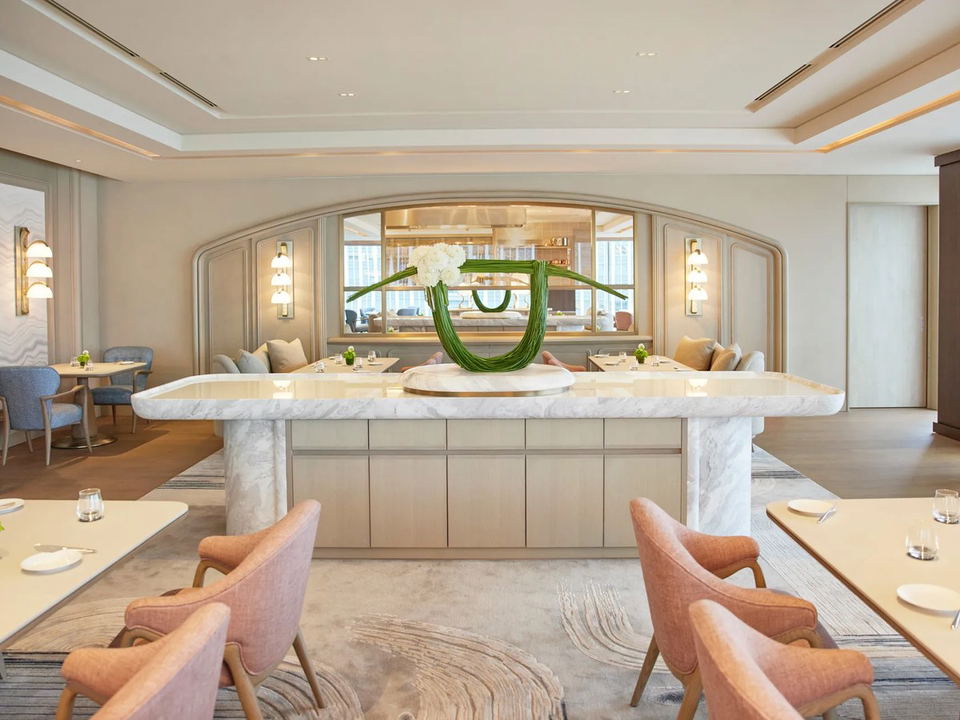 The dining room of Sézanne restaurant, featuring a central marble island with a sculptural floral arrangement, and elegant seating.