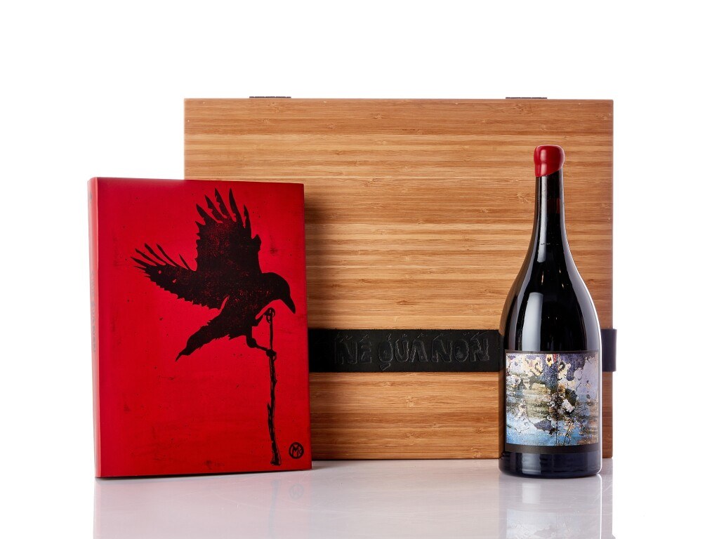 A red book with a black crow illustration, a bottle of Sine Qua Non wine, and a wooden box with 'Ne Qua Non' embossed.