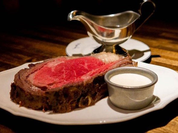 A thick slice of prime rib on a white plate, accompanied by a small ramekin of horseradish sauce and a silver gravy boat.