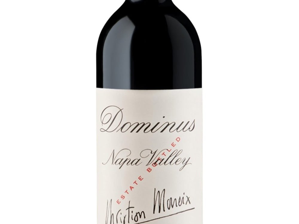 A bottle of Dominus Estate Napa Valley red wine with a red foil capsule, featuring a white label with 'Dominus Napa Valley' and 'Christian Moueix' in