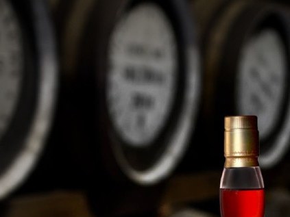 A bottle of Kavalan Solist Vinho Barrique single malt whisky and a tasting glass on a barrel in a dimly lit distillery warehouse.