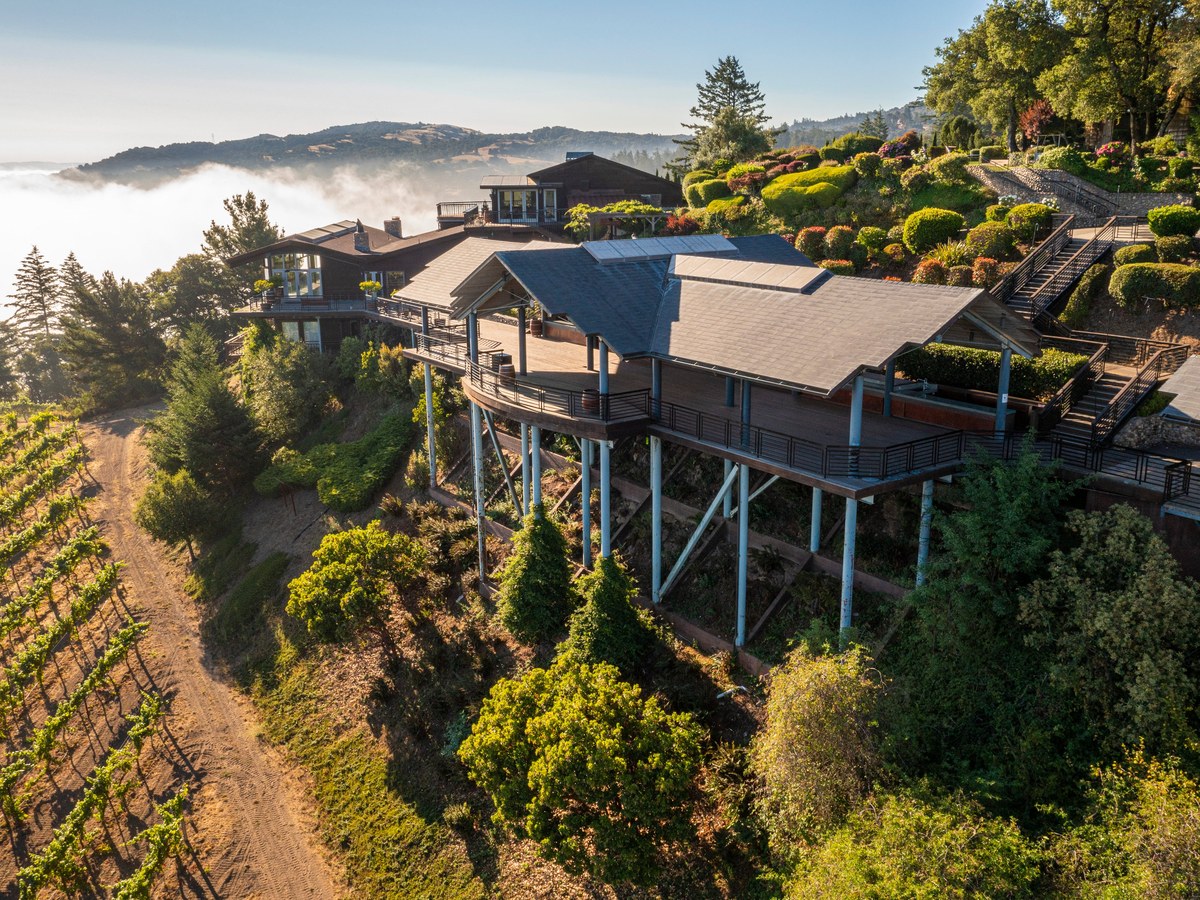 An aerial drone photograph shows the Thomas Fogarty Winery tasting room, with elevated decks on stilts, vineyards, and terraced gardens, overlooking