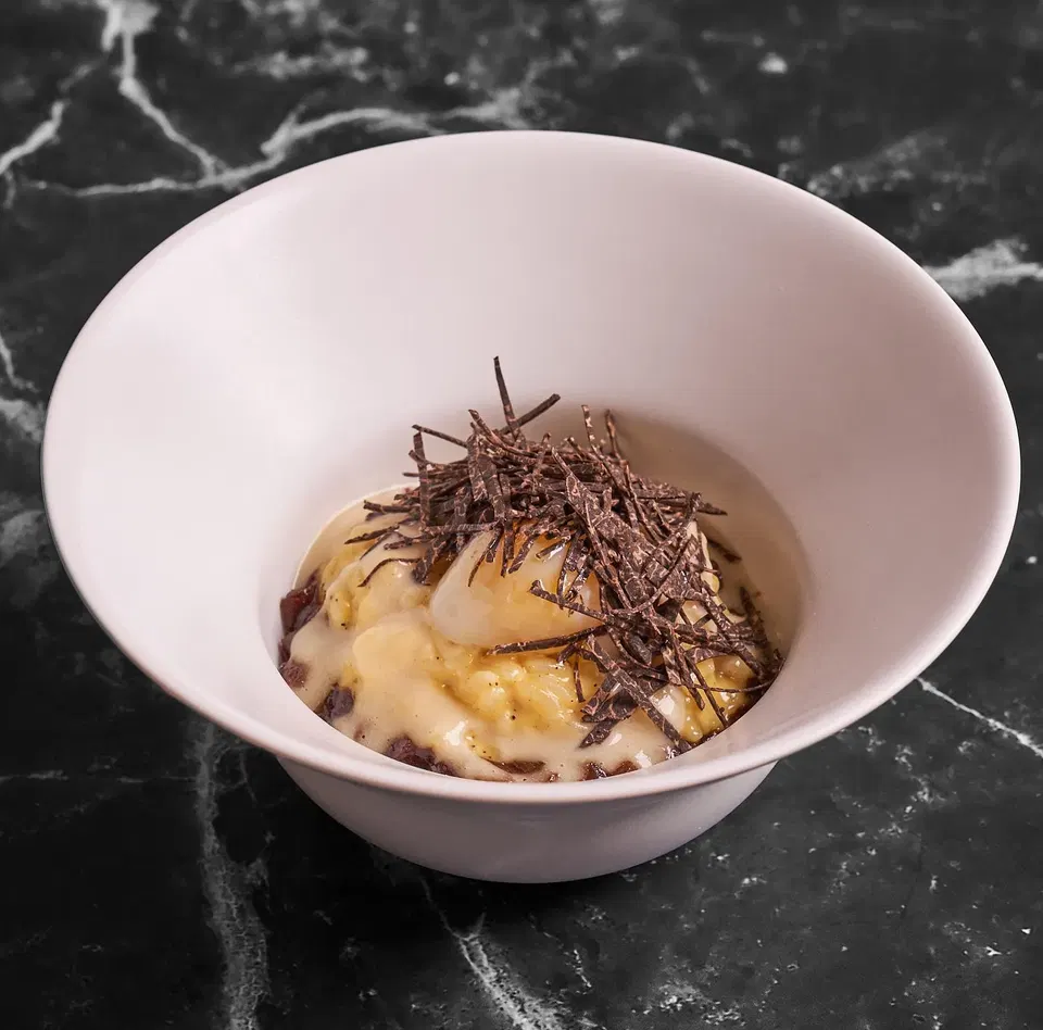 Creamy risotto topped with dark chocolate shards in a white bowl on black marble surface