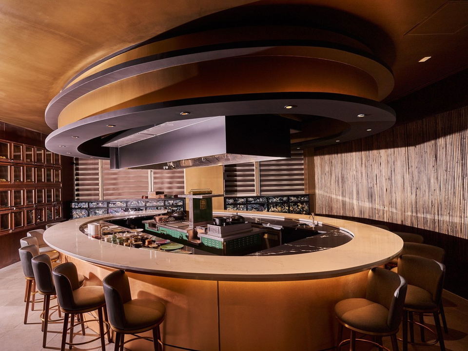 Hwaro's oval marble counter with warm brass under-lighting, surrounding an open kitchen.