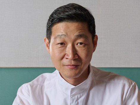 Sungchul Shim, Chef, GUI/Hwaro, sits at a wooden table with his hands clasped.