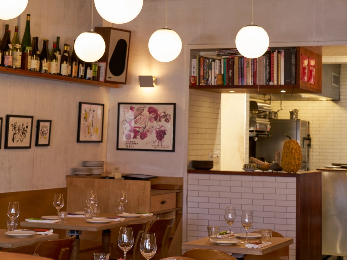 A modern dining room with wine bottles on display, set tables, and spherical pendant lights.
