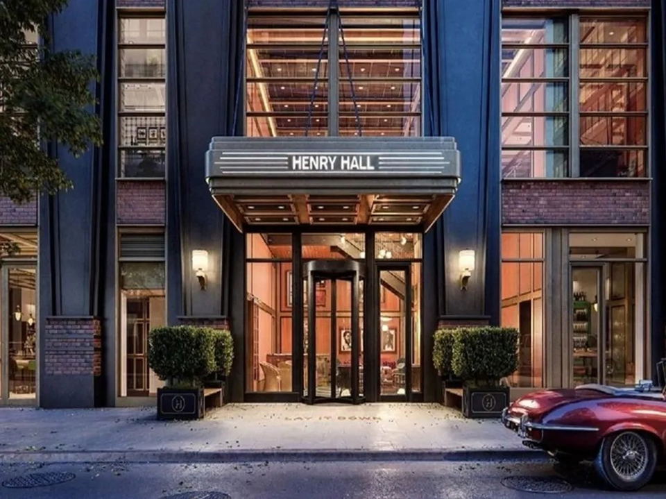 The exterior of Henry Hall, a building with a prominent sign, a revolving door, and a red car parked nearby.