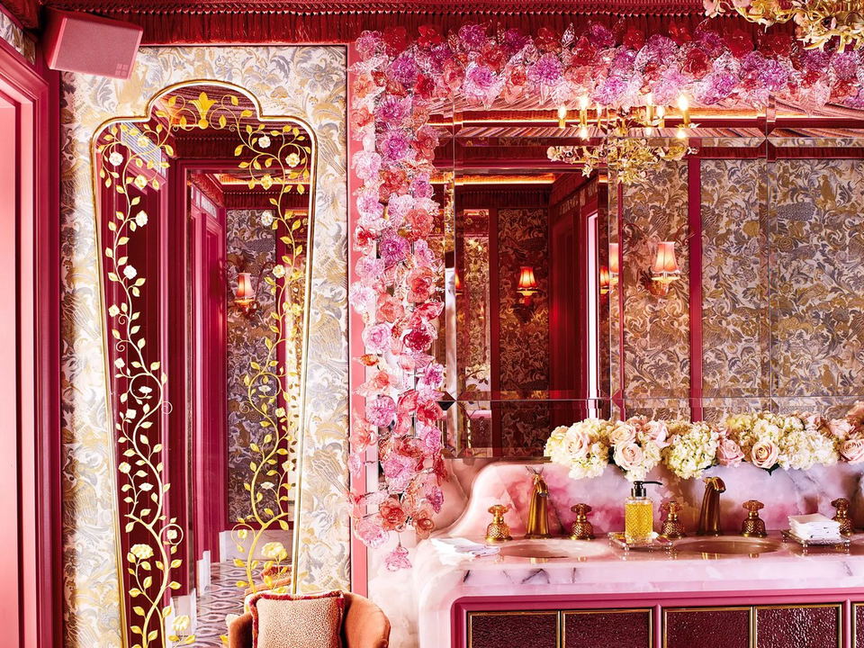 An opulent powder room at Annabel's Berkeley Square, featuring a draped crimson velvet ceiling, gold chandelier, floral mirror, and pink marble