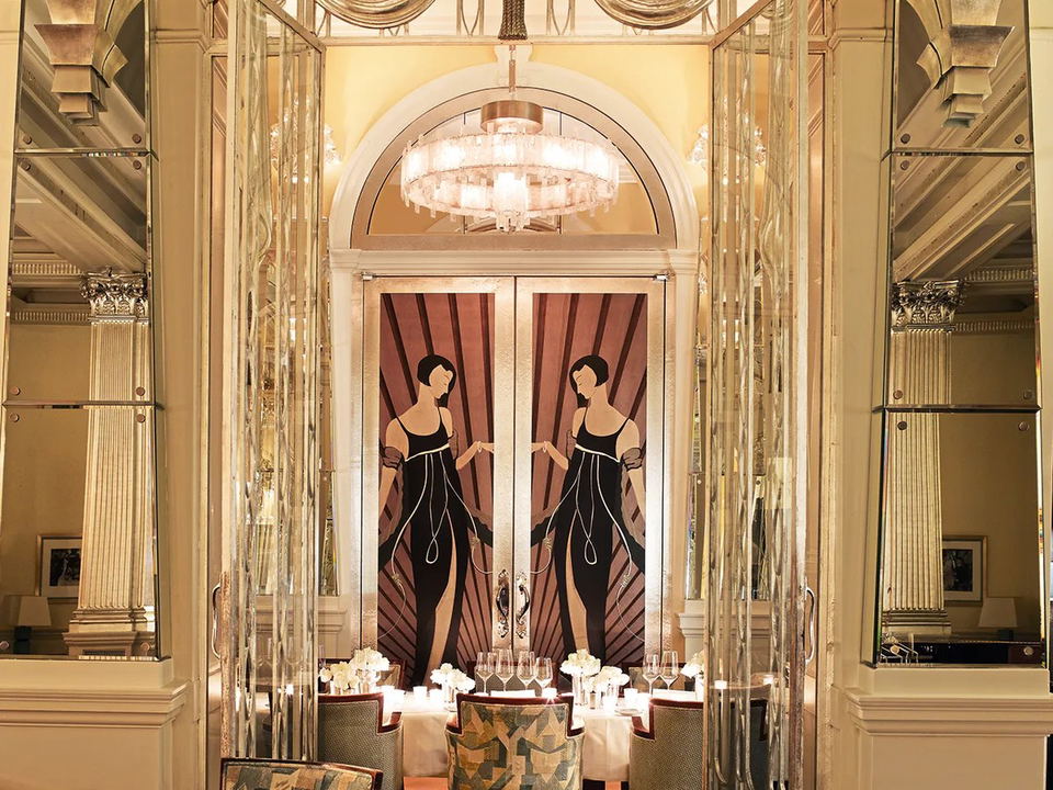 An Art Deco private dining room at Claridge's, featuring mirrored screens, an arched fanlight, a crystal chandelier, and stylized female figures on