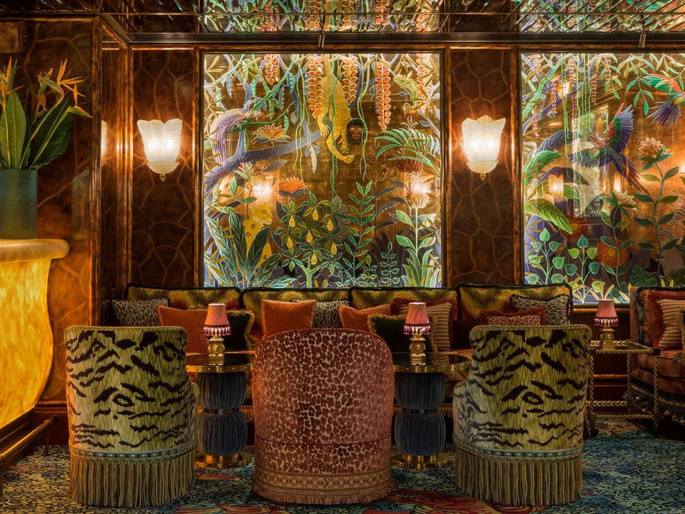 Leopard and tiger print tub chairs around brass side tables, set before a colourful botanical jungle mural with exotic birds, in a richly decorated Annabel's interior.