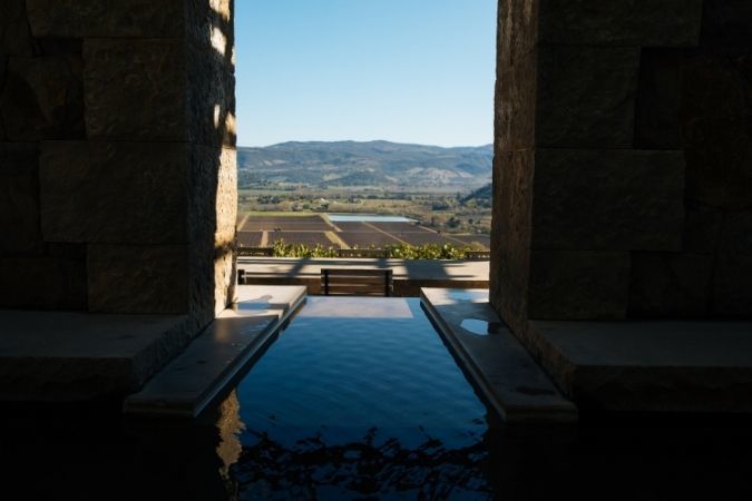 An infinity pool framed by stone pillars overlooking vineyard fields and mountains in Napa Valley