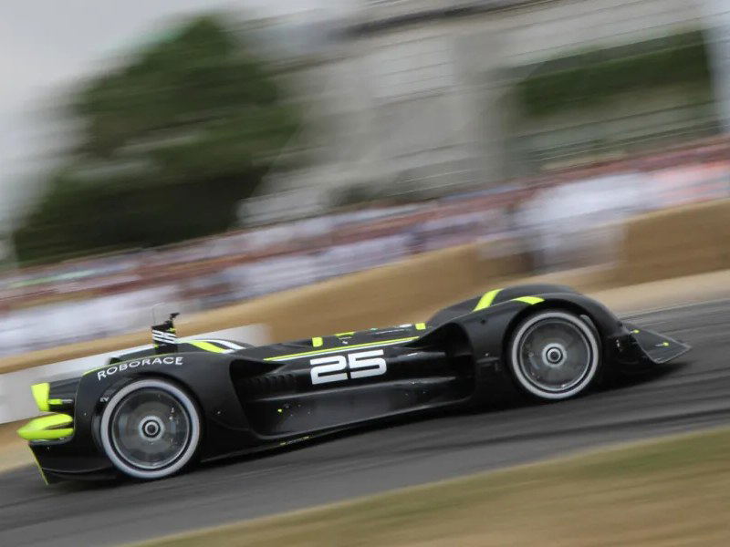 A black Roborace Robocar, number 25, speeds along the Goodwood Festival of Speed hillclimb driveway, with blurred crowds and trees in the background.