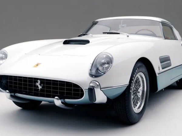 A classic white Ferrari concours car with light blue lower body accents, photographed in a studio setting, showcasing its elegant design.