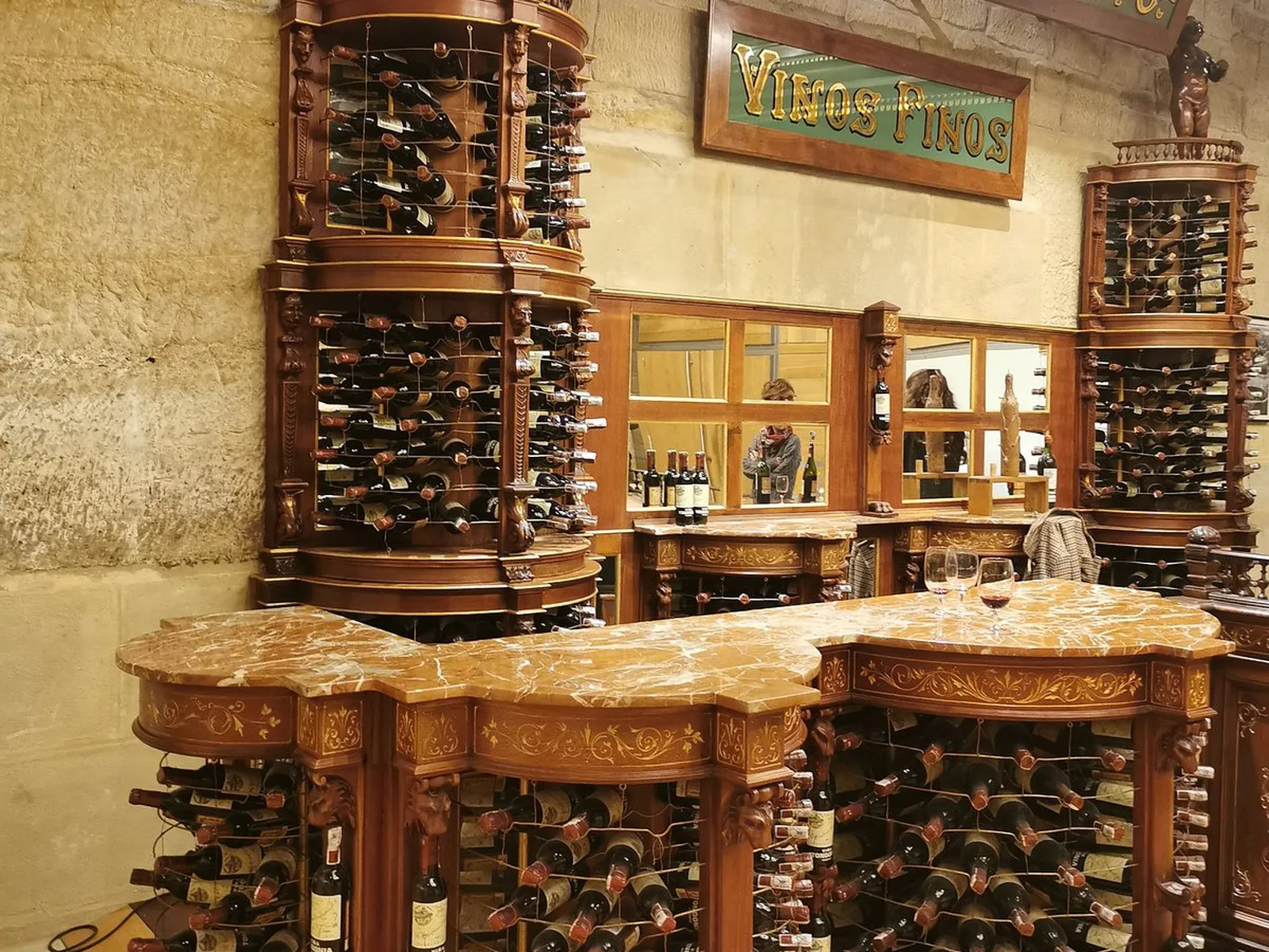 Interior of a luxury wine cellar with carved wooden wine racks, marble countertops, and a sign reading Vinos Finos on the wall.