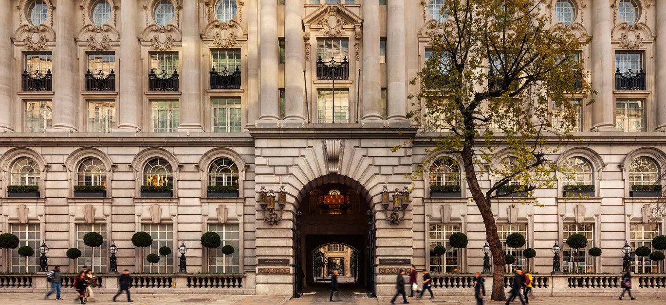 The Chancery Rosewood hotel's grand stone facade with arched windows, ornate balconies, and a large central archway, with people walking on the