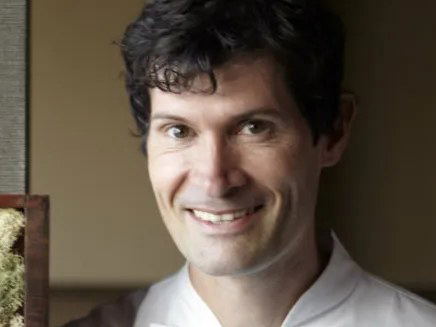 A chef in white chef's coat posing for a portrait in an interior setting with decorative moss/lichen wall art; source page (Eater) explicitly attests