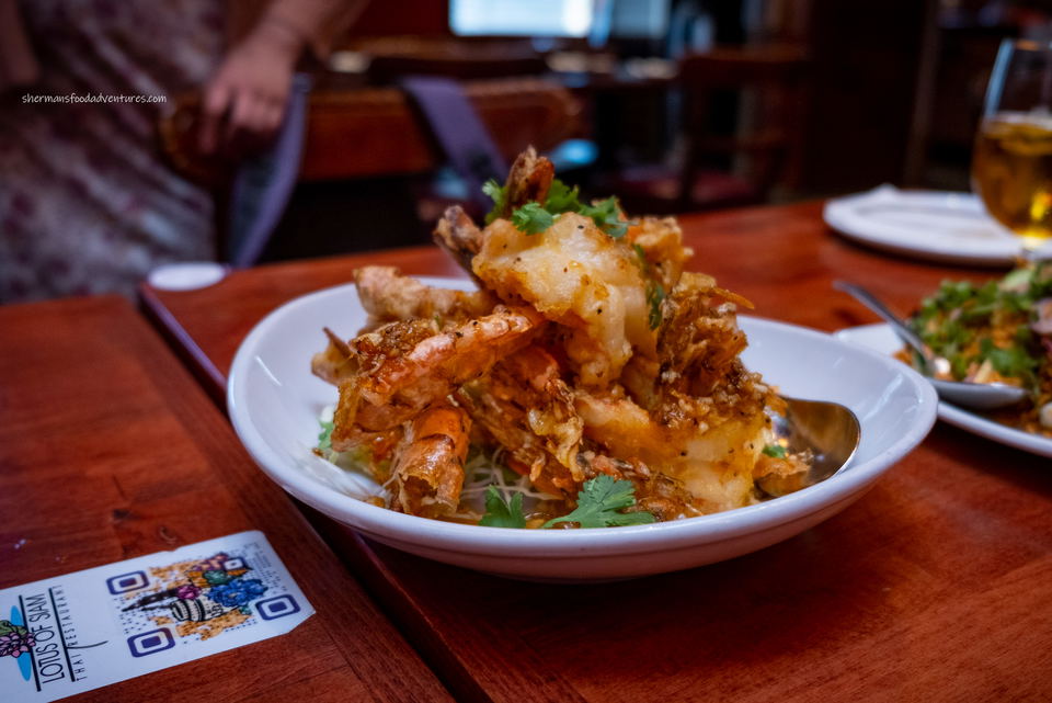 A white plate filled with crispy fried shrimp, garnished with fresh cilantro, sits on a wooden table at Lotus of Siam Thai Restaurant.