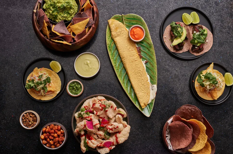 An overhead shot of a dark table laden with various Mexican dishes, including tacos, guacamole with chips, and other appetizers at Casa Playa.