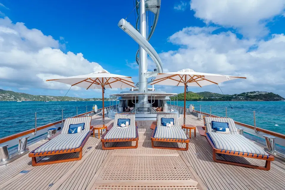 Luxury yacht deck with teak loungers, striped umbrellas, and turquoise Mediterranean waters under blue sky.