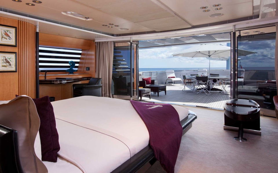 Luxurious master stateroom on the Maltese Falcon superyacht, with a king bed, wood-panelled walls, and open sliding glass doors leading to a private deck and the open sea.